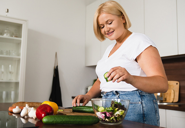 A woman standing at a kitchen counter with fresh produce in front of her after she lost weight with semaglutide in Fairfax, VA